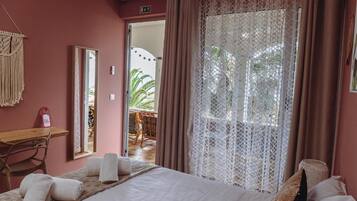 A hotel room with a bed, a desk, and a large window with lace curtains.