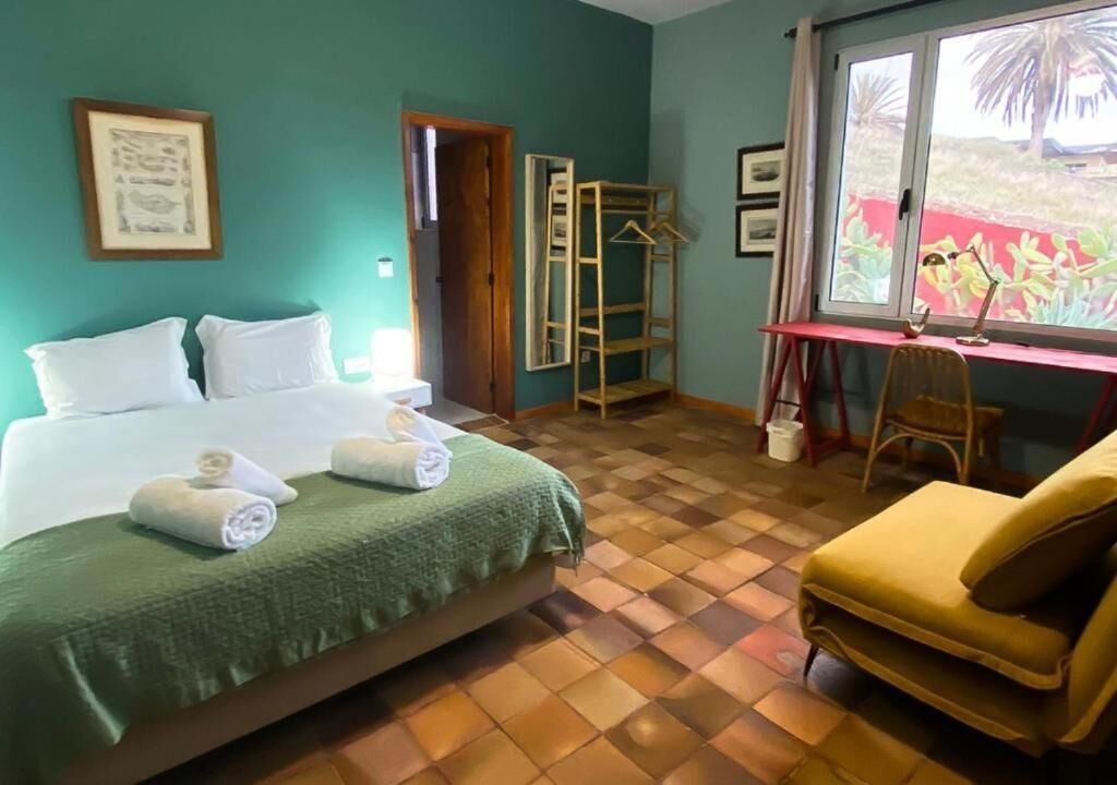 Habitación de hotel con cama, escritorio, silla y ventana con vistas a zonas verdes.