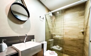 Un baño moderno con un lavamanos grande, un espejo y una ducha con mampara de vidrio.