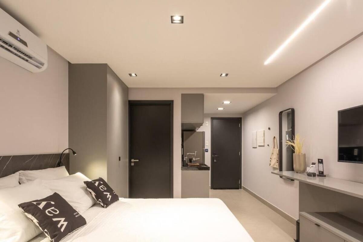 Une chambre d’hôtel moderne équipée d’un lit, d’une table de chevet, d’un climatiseur et d’un téléviseur fixé au mur.