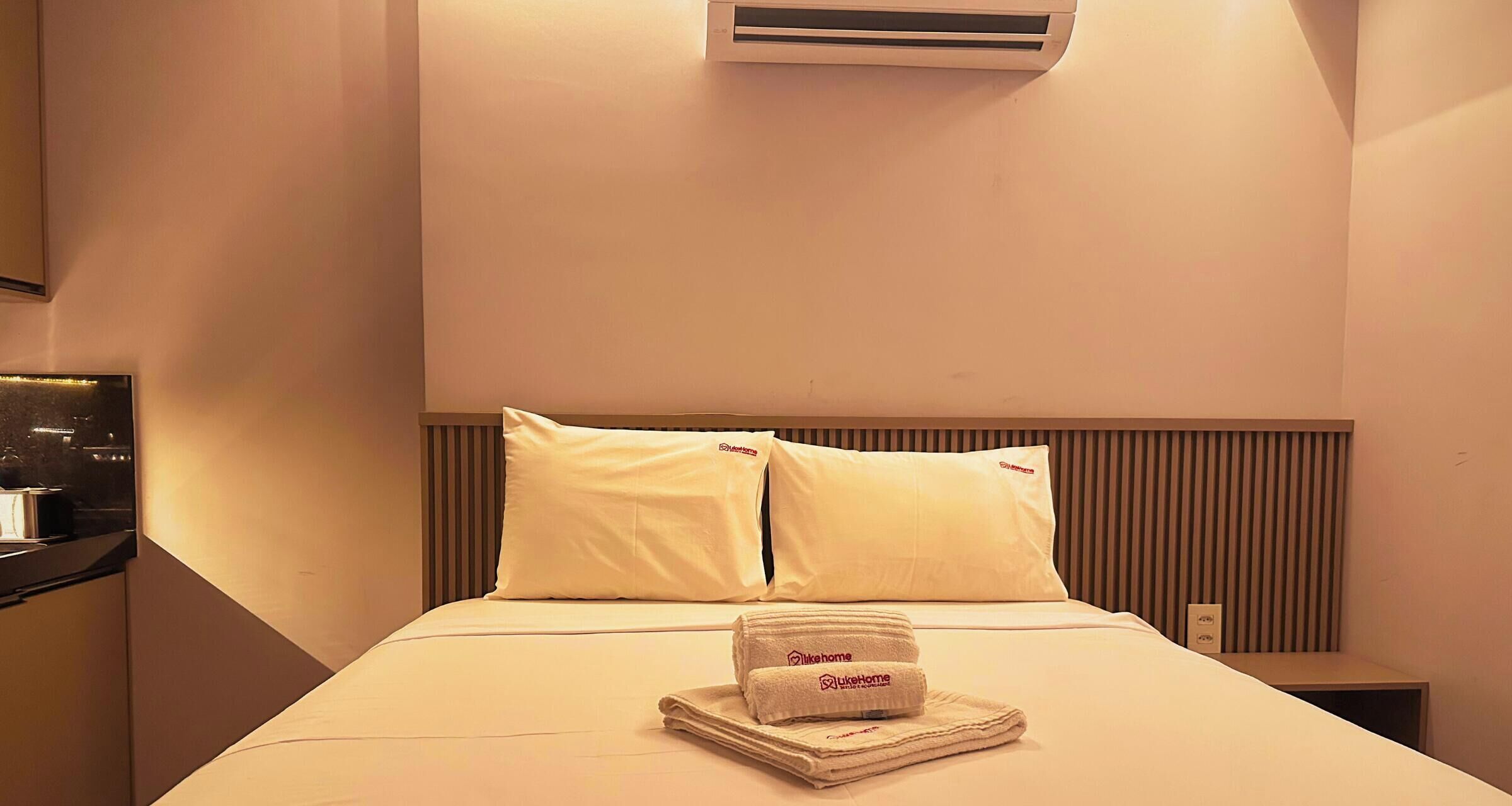 Une chambre d’hôtel avec un lit, des oreillers, une serviette pliée et un appareil de climatisation.