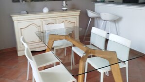 Un coin repas avec une table en verre et des chaises blanches, un buffet de couleur crème et un tableau accroché au mur.