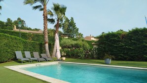 Une piscine entourée de trois chaises longues, avec une pelouse bien entretenue et des palmiers.