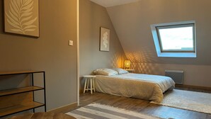 A bedroom with a bed, a small stool, a wooden table, and a window with a view.