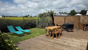 A wooden deck with a table and chairs, a barbecue grill, and two blue lounge chairs.