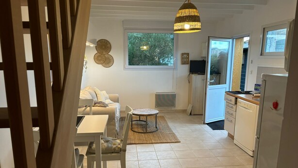 A modern kitchen with a dining area, a sofa, and a hanging light fixture.