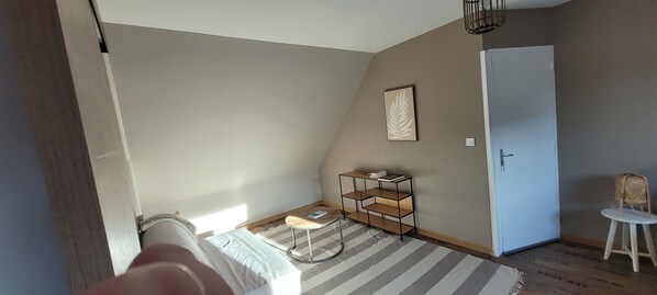A room with a bed, a small round table, a bookshelf, a chair, and a door.