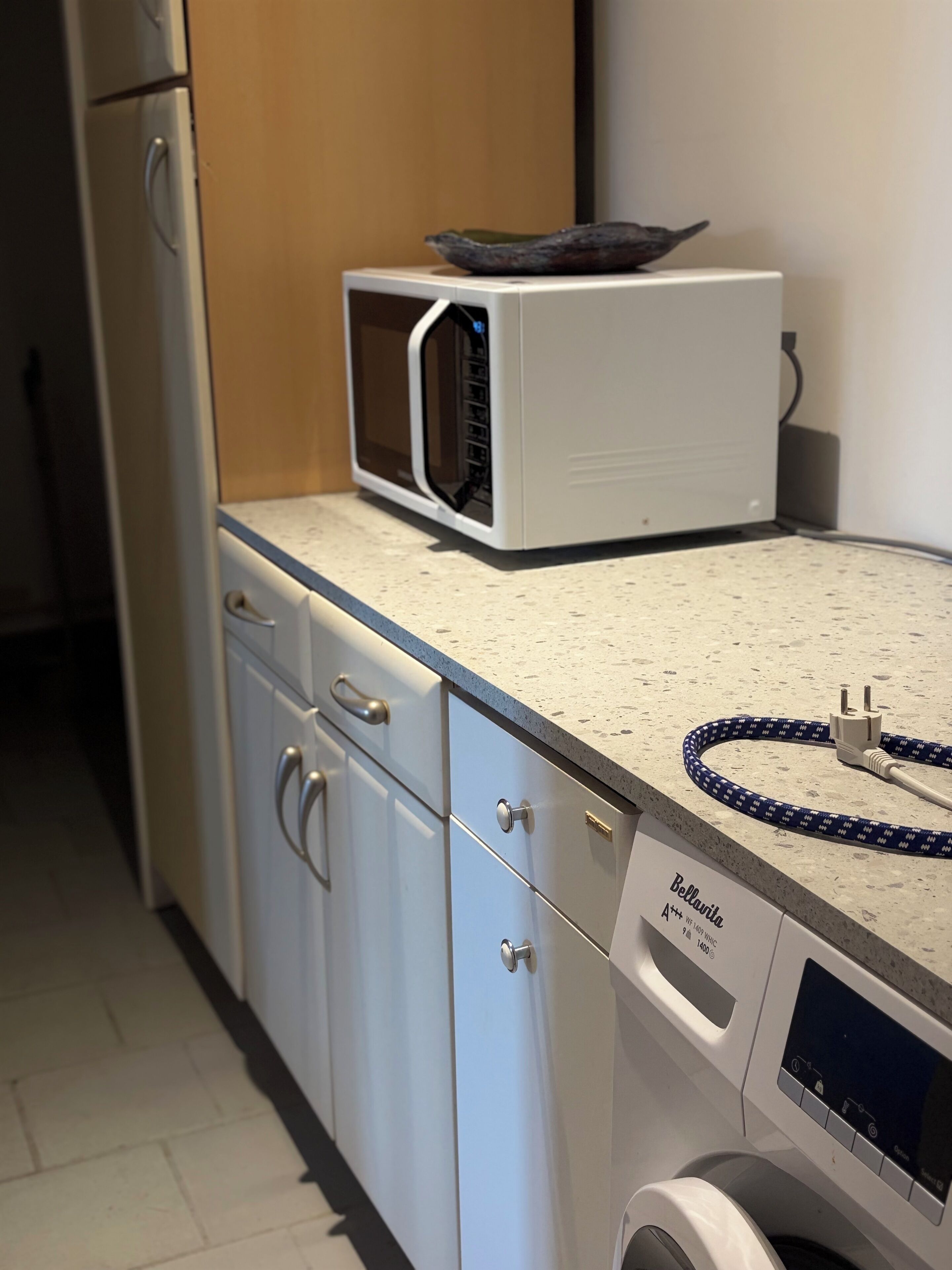 A kitchen with a microwave, a washing machine, and a dish rack.