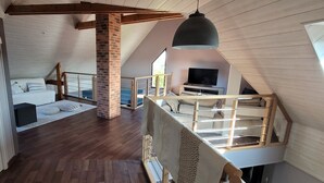 Un dormitorio estilo loft con techo de madera, columna de ladrillo, cama con ropa blanca, televisor y lámpara colgante.