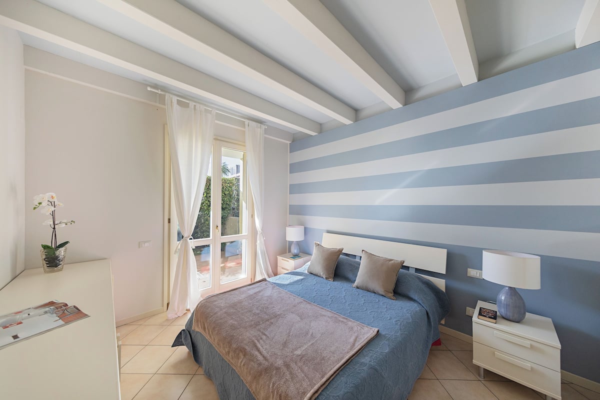 Une chambre à coucher avec un lit, des tables de chevet, une lampe et une vue par la fenêtre.