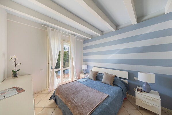 Un dormitorio con cama, mesitas de noche, una lámpara y vistas al exterior a través de una ventana.