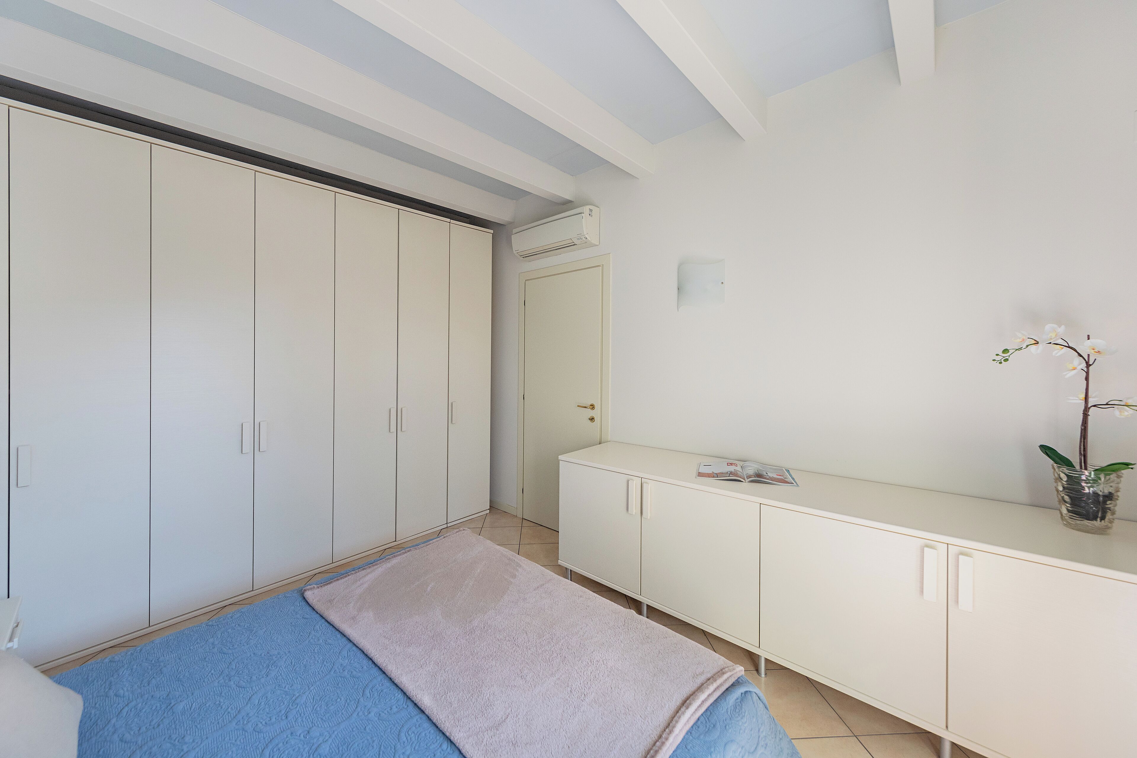 Une chambre à coucher avec un lit, une armoire, une coiffeuse avec un miroir et une petite plante.