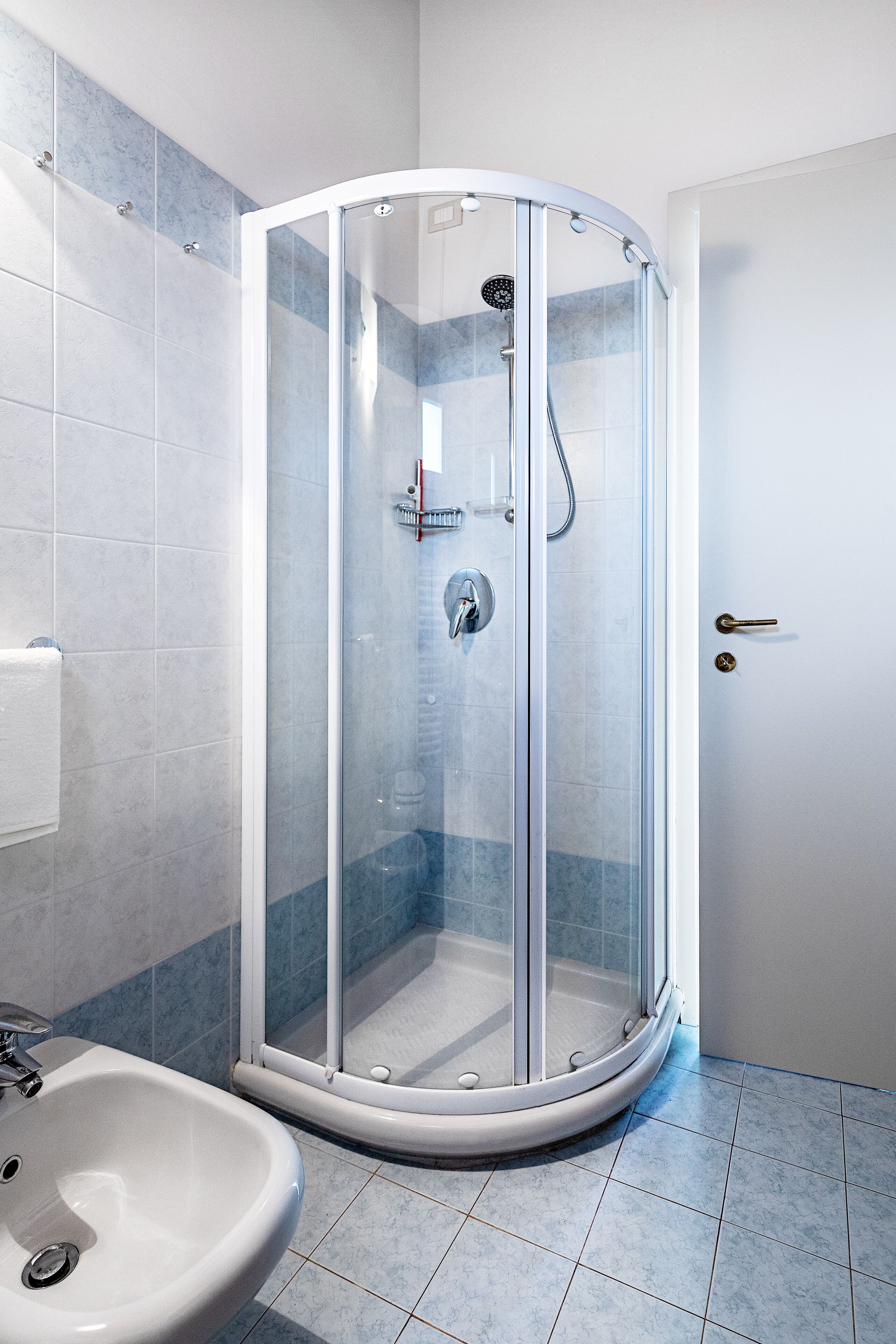 A modern bathroom with a glass-enclosed shower, a sink, and blue-tiled flooring.