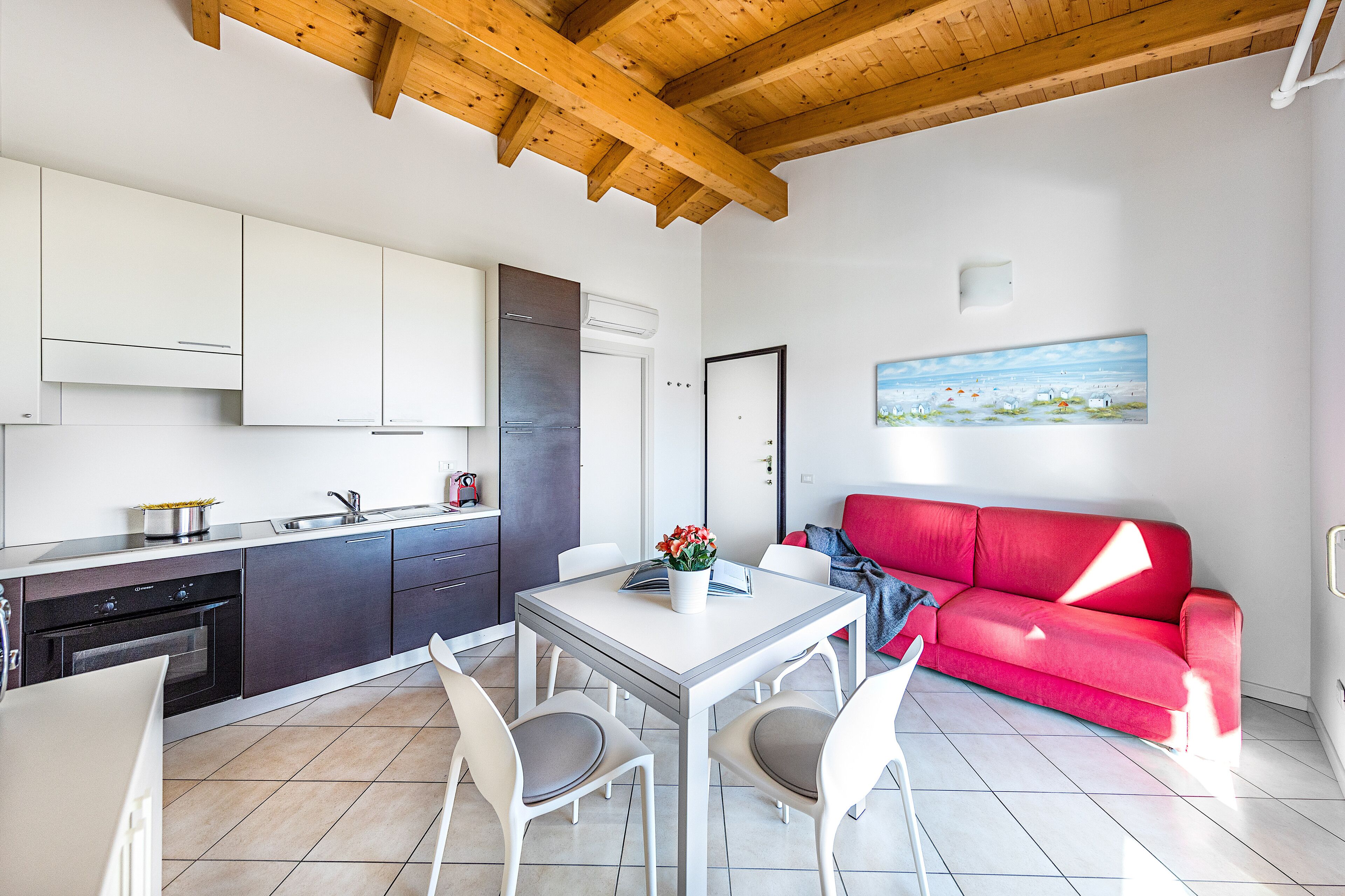 A modern kitchen with white cabinets, a dining table with chairs, and a red sofa in a bright living area.
