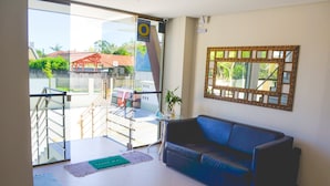 A lobby with a blue sofa, a glass door leading outside, a small table with a plant, and a decorative mirror on the wall. - Residencial Canto dos Passaros (Florianópolis)