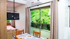 A room with a dining table, chairs, a TV mounted on the wall, and a window with curtains. - Residencial Canto dos Passaros (Florianópolis)