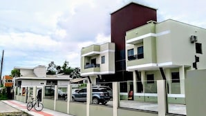 A modern building with multiple floors, large windows, and a parking area with cars and a bicycle. - Residencial Canto dos Passaros (Florianópolis)