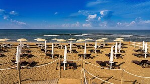 A beach with rows of sun loungers and umbrellas, a wooden deck, and the ocean in the background. - Cozy villa with pool nestled among the ancient olive trees of Cilento  (Capaccio Paestum)