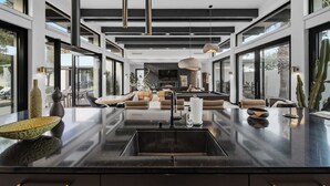 Une cuisine moderne dotée d’un îlot central, de plans de travail noirs et de luminaires suspendus.
