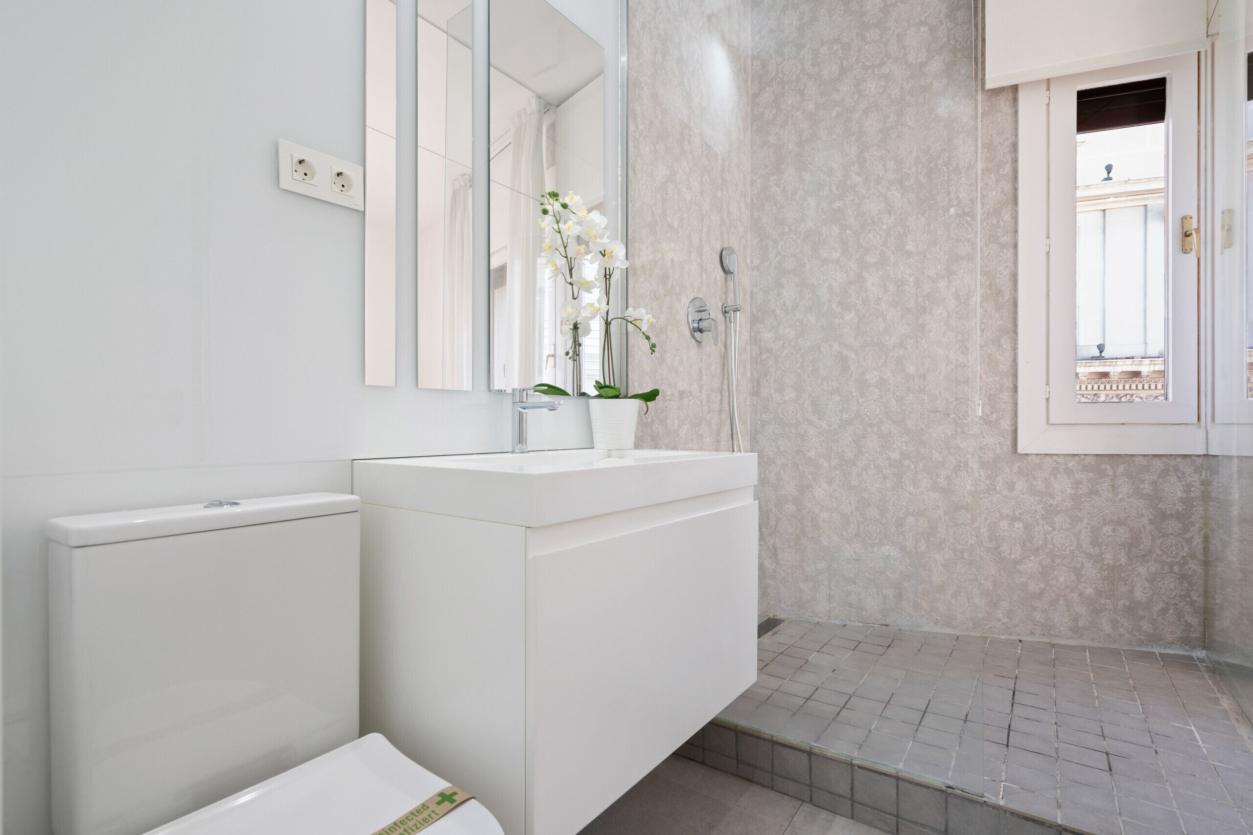 Une salle de bain moderne avec un meuble-lavabo blanc, un miroir, une douche et une vue sur l’extérieur.