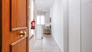 Ein Korridor mit einer Holztür, einem weißen Kühlschrank, einem kleinen Tisch mit Lampe und einem beigefarbenen Sofa.