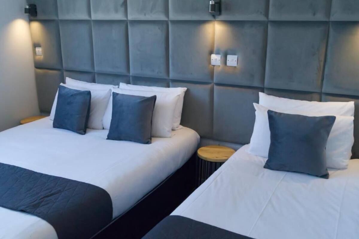 Une chambre d’hôtel avec deux lits, chacun doté de draps blancs et d’oreillers gris. La tête de lit est rembourrée et agrémentée d’appliques murales.