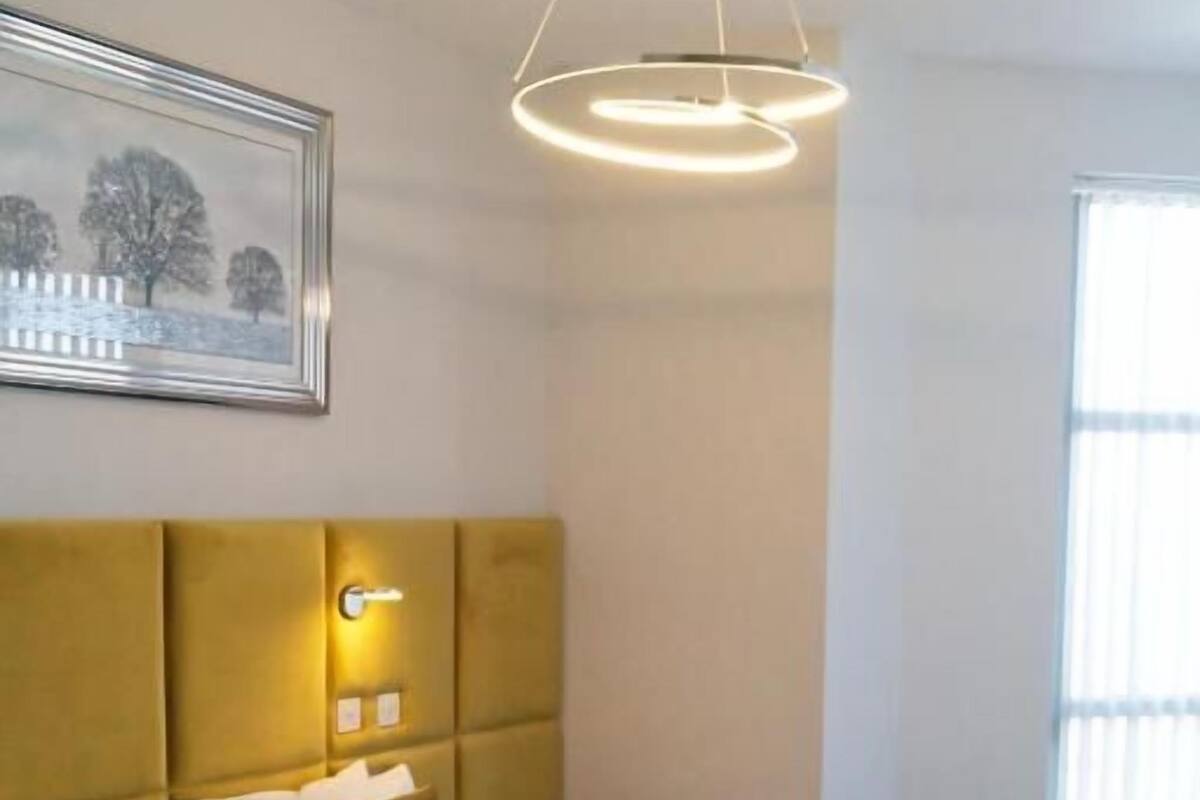 Une chambre d’hôtel avec un grand lit, une tête de lit dotée d’un éclairage intégré, une table de chevet et un tableau encadré au mur.