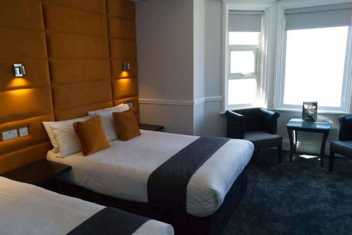 Une chambre d’hôtel avec deux lits, un canapé, une petite table et une fenêtre avec des stores.