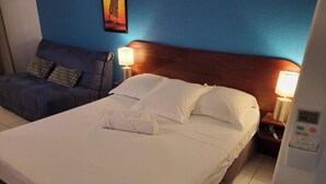 Habitación de hotel con cama, sofá, dos lámparas y mesita de noche con panel de control.