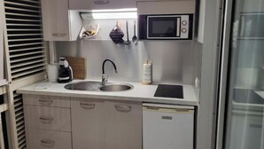 Una kitchenette compacta con un lavamanos, un microondas y un refrigerador pequeño.