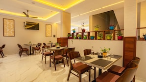 A modern dining area with marble flooring, wooden tables and chairs, ceiling fans, and potted plants. - Treebo Grand Royal Imperio, Hinjewadi (Paud)