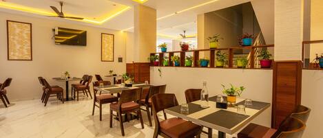 A modern dining area with marble flooring, wooden tables and chairs, ceiling fans, and potted plants.