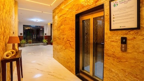 A hotel lobby with a marble floor, a reception desk with a lamp, a framed sustainability guide, and an elevator. - Treebo Grand Royal Imperio, Hinjewadi (Paud)