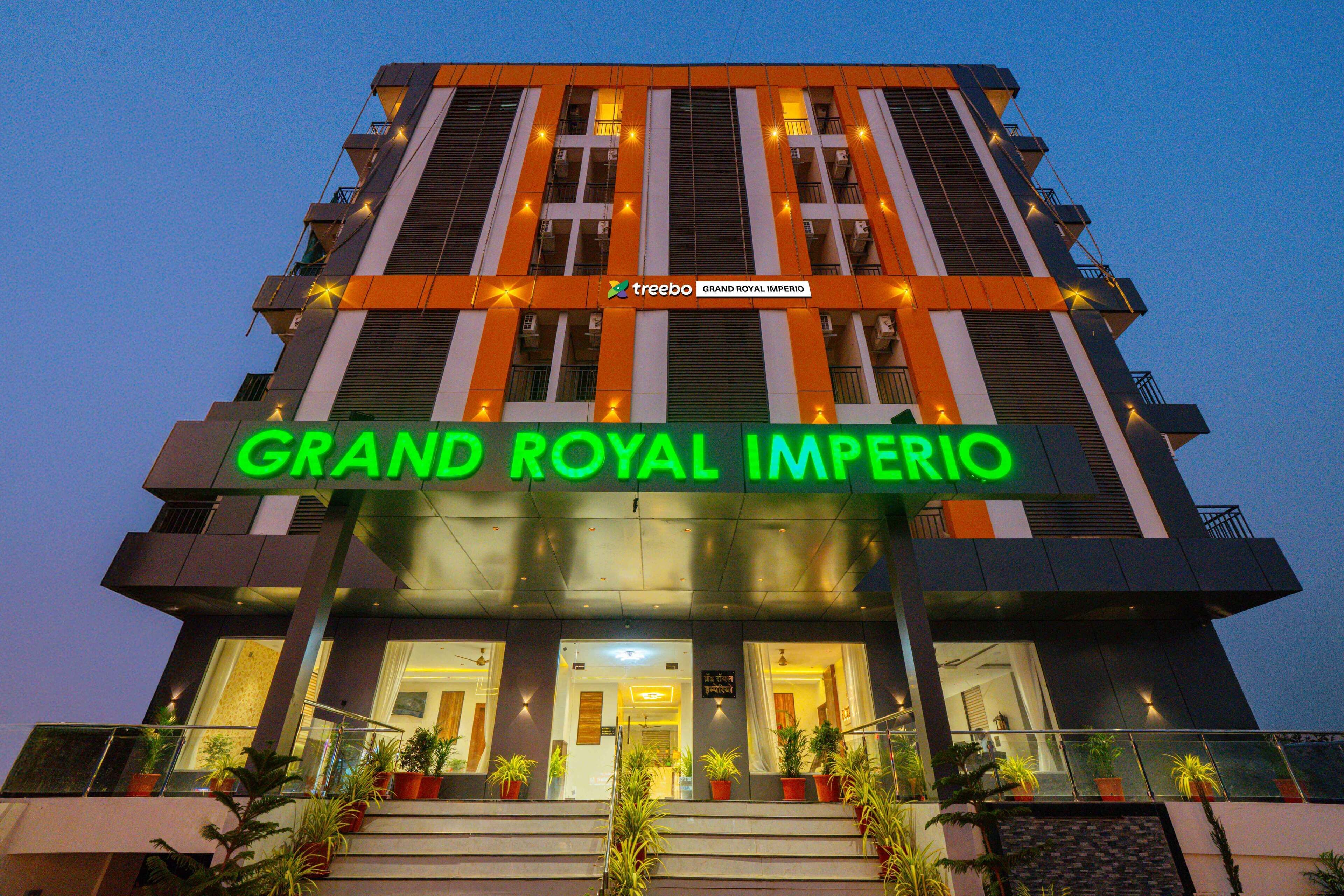 Un hotel con un llamativo letrero que dice "Grand Royal Imperio", varios pisos y plantas en macetas en la entrada.