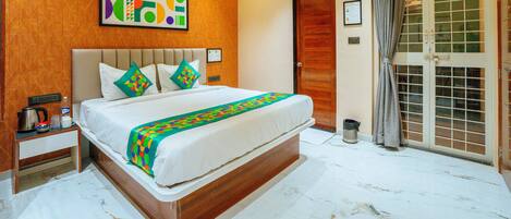 Habitación de hotel con cama, ventilador de techo, aire acondicionado en la pared, puerta con vistas y una mesita con tetera y tazas.