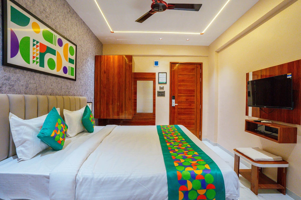 Una habitación de hotel con cama, ventilador de techo, televisión y puerta de madera.