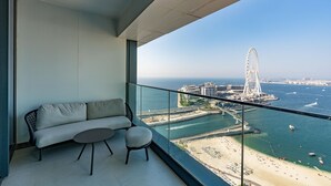 A balcony with a sofa and chairs, overlooking a coastal cityscape with a prominent Ferris wheel.