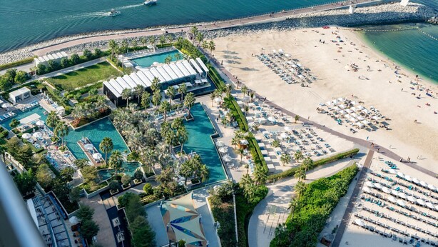 A resort with multiple swimming pools, a beach area with sun loungers, and a rocky shoreline.
