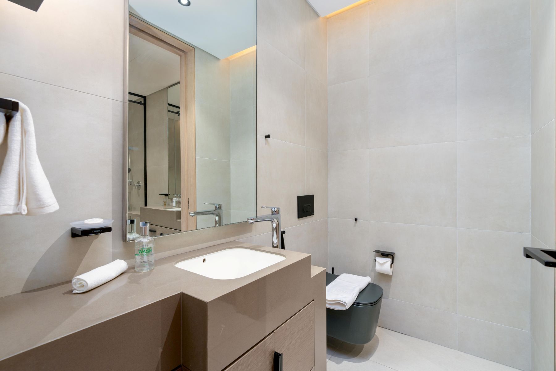 A modern bathroom with a large mirror, a sink, and a toilet.