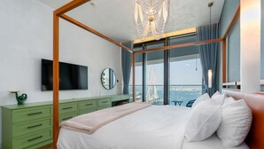 A modern bedroom with a four-poster bed, a television, a green dresser, and a large window offering a view of a Ferris wheel.
