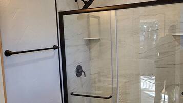 A bathroom with a wooden ceiling, a glass shower enclosure, a white toilet, and a black sink.