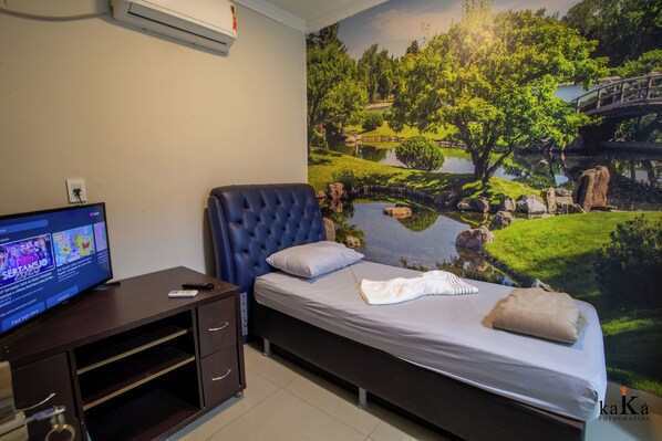 A bedroom with a bed, a TV on a desk, and a mural of a landscape.