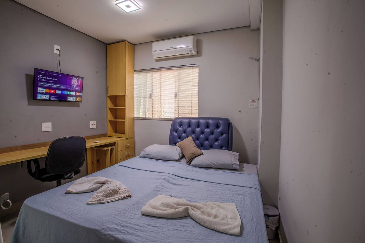 A bedroom with a bed, a desk, a chair, and a television mounted on the wall.