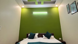 Un dormitorio con cama, paredes verdes, ventilador de techo, iluminación empotrada y cuadros enmarcados.