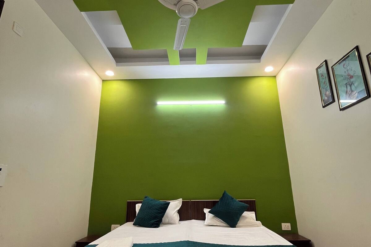 A bedroom with a bed, green walls, a ceiling fan, recessed lighting, and framed artwork.