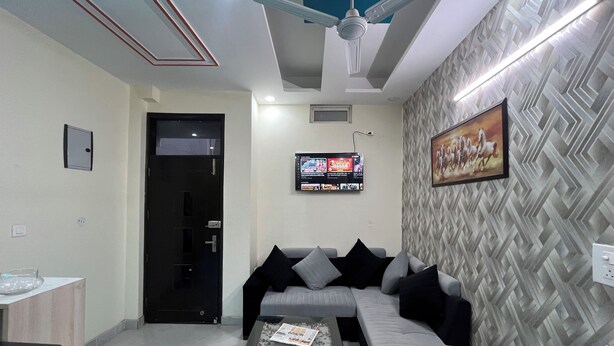Una sala de estar moderna con un sofá gris, cojines negros y grises, una mesa de centro con revistas, un televisor montado en la pared y un papel tapiz estampado.