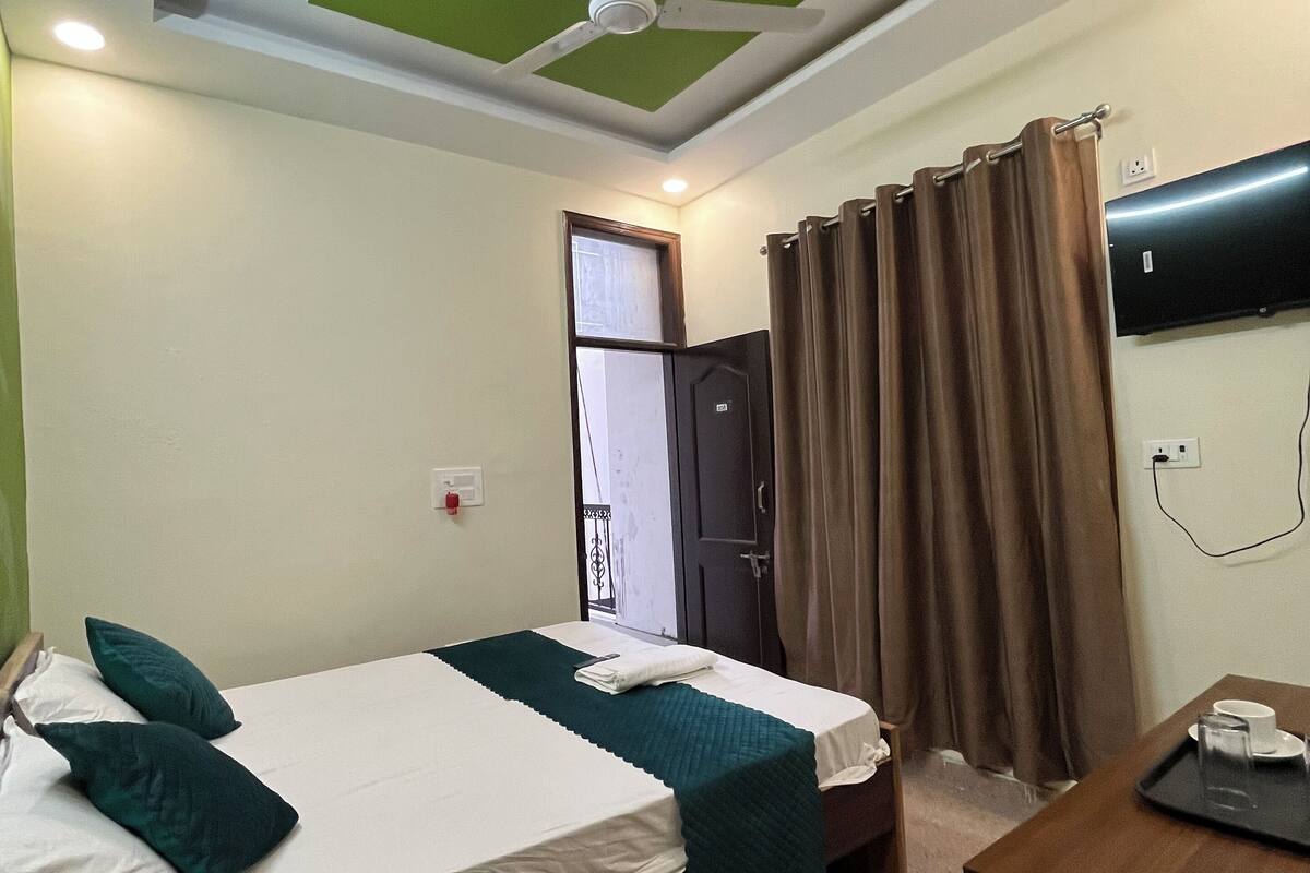 A hotel room with two beds, a ceiling fan, a desk with a tray, and a window with curtains.