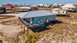 A coastal house with a metal roof, a deck with outdoor furniture, and a small porch. - Sand Digs! Adorable Gulf Beachside, 2 Bedroom, 2 Bath, Pet Friendly! (Dauphin Island)