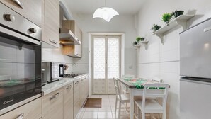 A modern kitchen with white cabinets, a built-in oven, and a dining area with a table and chairs. - Cozy 2-Bedroom Flat with Balcony (Rome)