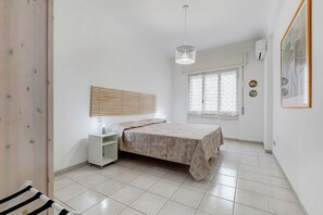 A bedroom with a bed, bedside table, hanging light fixture, window, and a wall-mounted air conditioner. - Cozy 2-Bedroom Flat with Balcony (Rome)